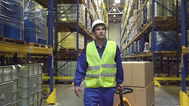 Cheerful warehouse worker moves cart with boxes