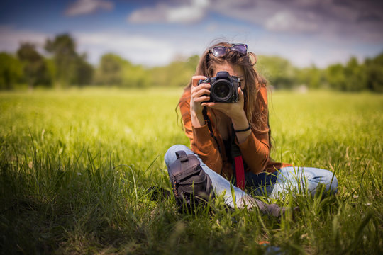 Young woman, professional photographer, taking pictures of a beautiful nature surrounding her, warm sunny day
