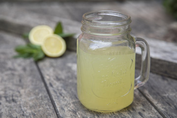 Lemon juice in jar, decorated with fresh lemons and mint leaves.