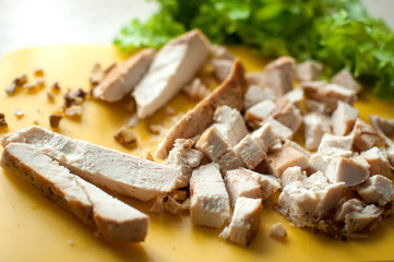 Chopped ruddy chicken breasts with leaf salad and crushed walnut on yellow cutting board.