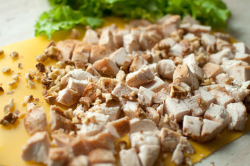 Chopped ruddy chicken breasts with leaf salad and crushed walnut on yellow cutting board.
