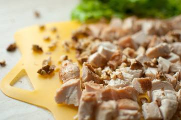 Chopped ruddy chicken breasts with leaf salad and crushed walnut on yellow cutting board.