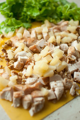 Chopped ruddy chicken breasts with leaf salad and crushed walnut on yellow cutting board.
