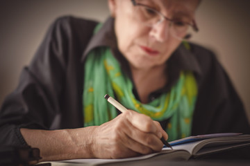 Senior old woman writing down letters on a piece of paper, recording a journal or diary entry or...