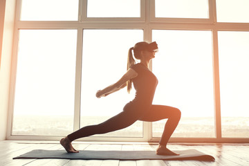 A young beautiful woman in virtual reality glasses makes aerobics remotely. Future technology...
