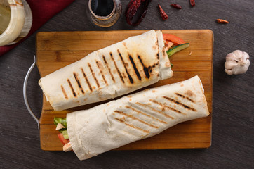 Shaurma chicken roll in a pita with fresh vegetables and cream sauce composition on wooden background