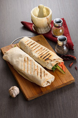 Shaurma chicken roll in a pita with fresh vegetables and cream sauce composition on wooden background