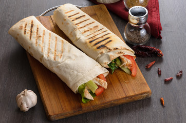 Fototapeta na wymiar Shaurma chicken roll in a pita with fresh vegetables and cream sauce composition on wooden background