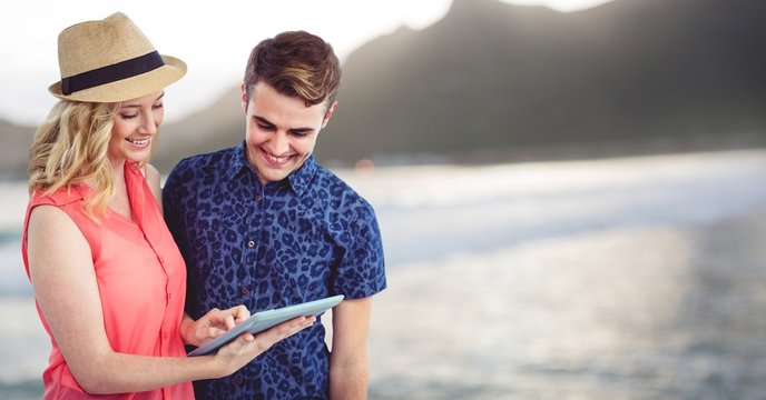 Trendy man and woman with tablet against blurry coastline