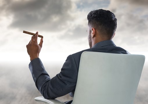 Back Of Seated Business Man Smoking Cigar And Looking At Clouds