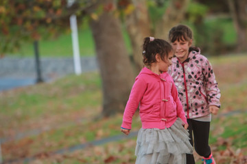 outdoor portrait of two young happy children, girls - sisters - playing in park on natural background