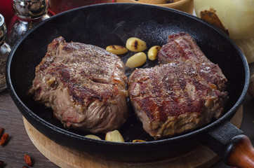 Grilled rib eye steak composition on grill iron pan on wooden background