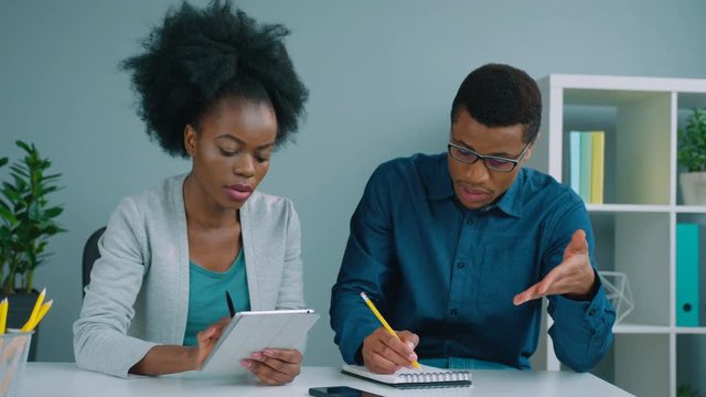 Team of two african american business people working together at the office. African American businessman and businesswoman talking, using tablet device, checking financial charts.