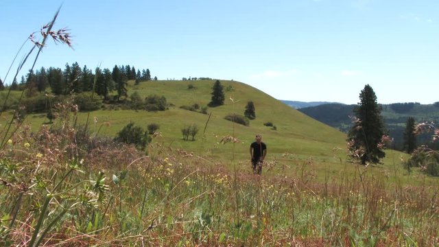 Model released man walks up hill through Oregon meadow on clear and peaceful day.