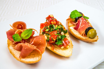 Delicious, mouth-watering different canapes with meat, vegetables, herbs and olives, on a white plate. Horizontal frame
