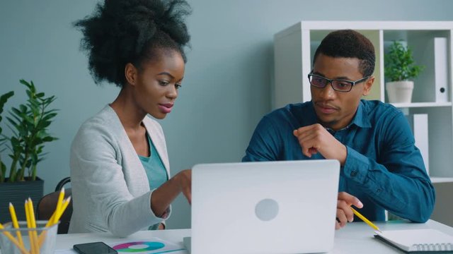 Two african american business people working together at the office. African American businessman and businesswoman talking, using laptop computer, checking financial charts.