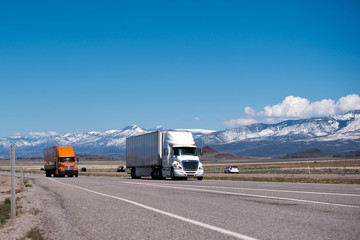 White and orange semi trucks and trailers on high way