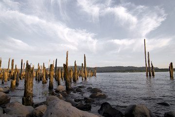 Wooden poles old pier destroyed by time and boulders on Columbia River