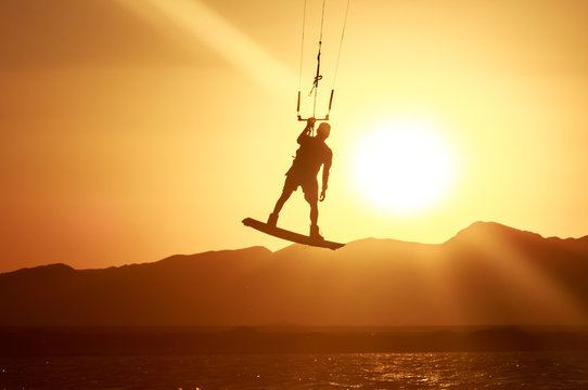 Kiteboarder sportsman with kite under sunset sun, freestyle kiteboarding rider on the evening kitesession, sunset in the sea, extreme watersports, active lifestyle, recreational hobby and fun time