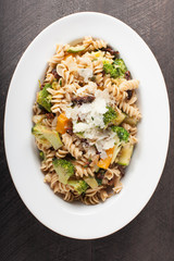  
Large White Bowl of cooked pasta topped with sundried tomatoes, bell peppers, broccoli, and parmesan cheese above shot
