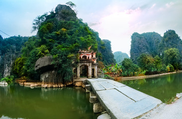 Outdoor park landscape with stone bridge and lake. Gate entrance to old Bich Dong pagoda complex. Ninh Binh, Vietnam - travel destination.
