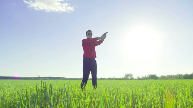 Businessman with a gun on a green wheat field looks around and shoots