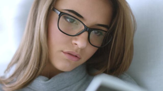 Close up view of attractive young brunette girl in glasses relaxing at home on the armchair reading a book