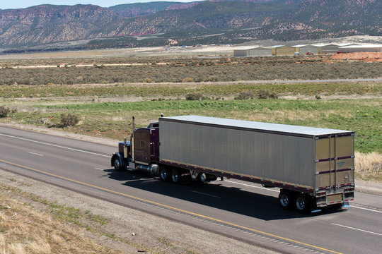 Dark Classic semi truck and trailer on the road with nature view