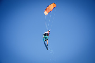 Professional kite boarding rider sportsman with kite in sky jumps high acrobatics kiteboarding trick with grab of kiteboard and huge water splash. Recreational activity, extreme active air sports