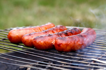  Four grilling sausages on barbecue grill. Selective focus