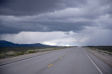 Road stretches into horizon with stormy sky and snow-capped mountains