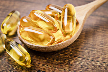 Fish oil capsules with omega 3 and vitamin D in a wooden spoon.