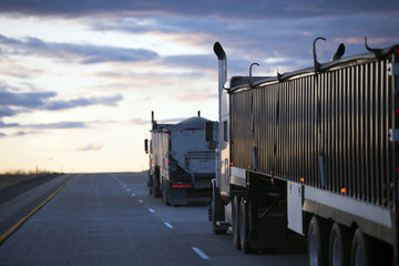 Evening road uphill with convoy semi trucks with bulk trailers