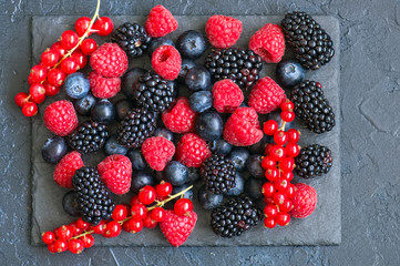 Berry raspberries red currants and blueberries on black slate board. Gray stone background.  Top view.