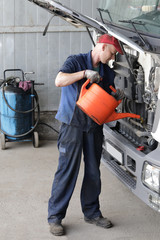 The mechanic pours engine oil into the engine of the truck