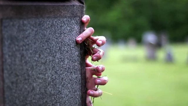 Zombie hands coming up frombehind graveyard headstone - creepy halloween concept