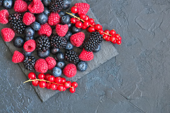 Berry raspberries red currants and blueberries on black slate board. Gray stone background.  Top view.