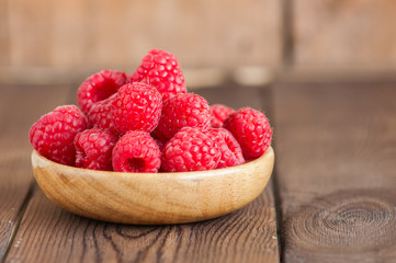 Close up of heap of ripe red sweet raspberries in a wooden plate. Wooden background.