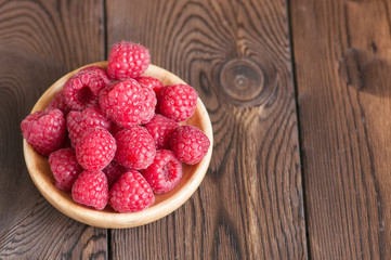 Close up of heap of ripe red sweet raspberries in a wooden plate. Wooden background.