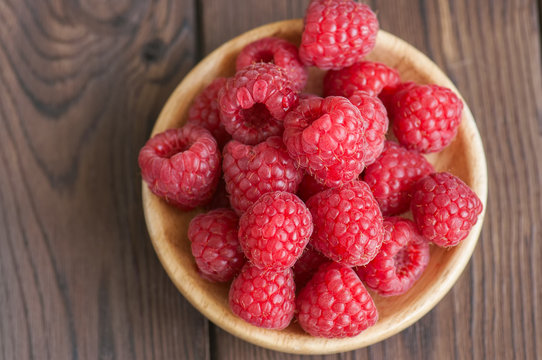 Close up of heap of ripe red sweet raspberries in a wooden plate. Wooden background. Top view