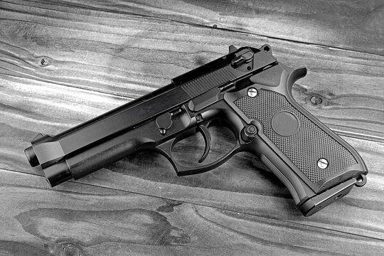 Weapon series. Modern U.S. Army handgun M9 close-up on grey wooden background. (Black & White)