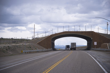 Semi trucks going under small arched pedestrian bridge