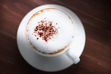 Cappuccino coffee with cacao topping in white cup over dark rustic wooden background