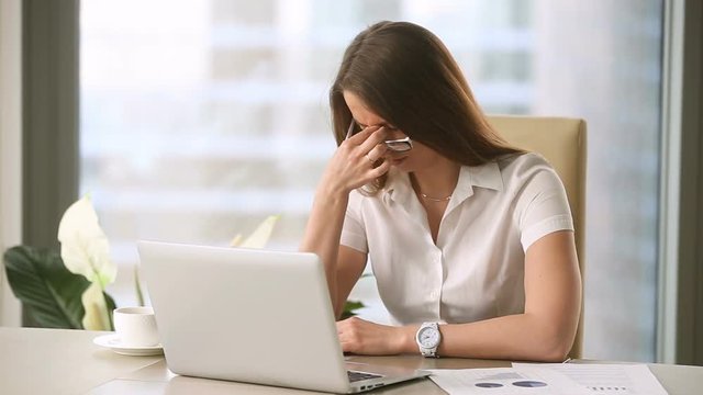 Young businesswoman taking off glasses while working on laptop at office, feeling discomfort and eye strain after long wearing, massaging nose bridge, blurry irritated dry eyes, eyesight problems