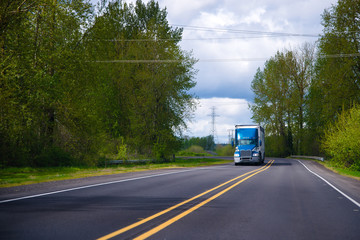 Fototapeta na wymiar Blue big rig semi truck on green road with trees