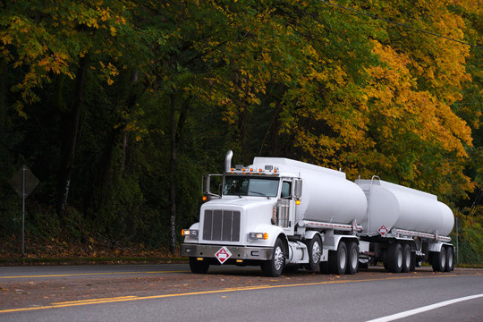 White big rig semi truck with two tank trailers on autumn road