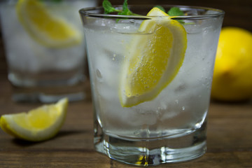 Refreshing beverage with lemon, ice and mint leaves in glass, isolated on wooden background. Closeup