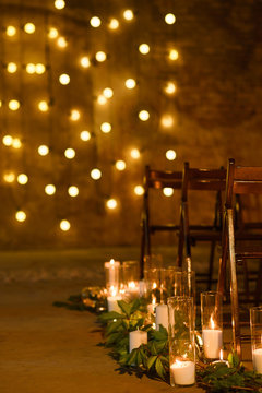 Wedding ceremony decorations in loft grunge surround. Light bulb garland, candles, glass and chairs