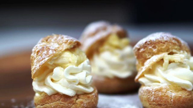 Bakery pastry chef sprinkling powdered sugar choux cream puff on wood board 4k