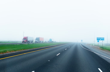 Foggy road with convoy of semi trucks with trailers